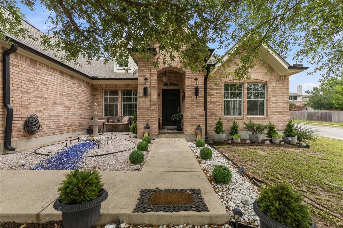 2501 Aspen Meadow Road Leander, TX 78641 - Photo 2 of 30 Brick facade residence featuring an arched entry, multiple windows, a concrete walkway, and landscaped rock beds with plantings