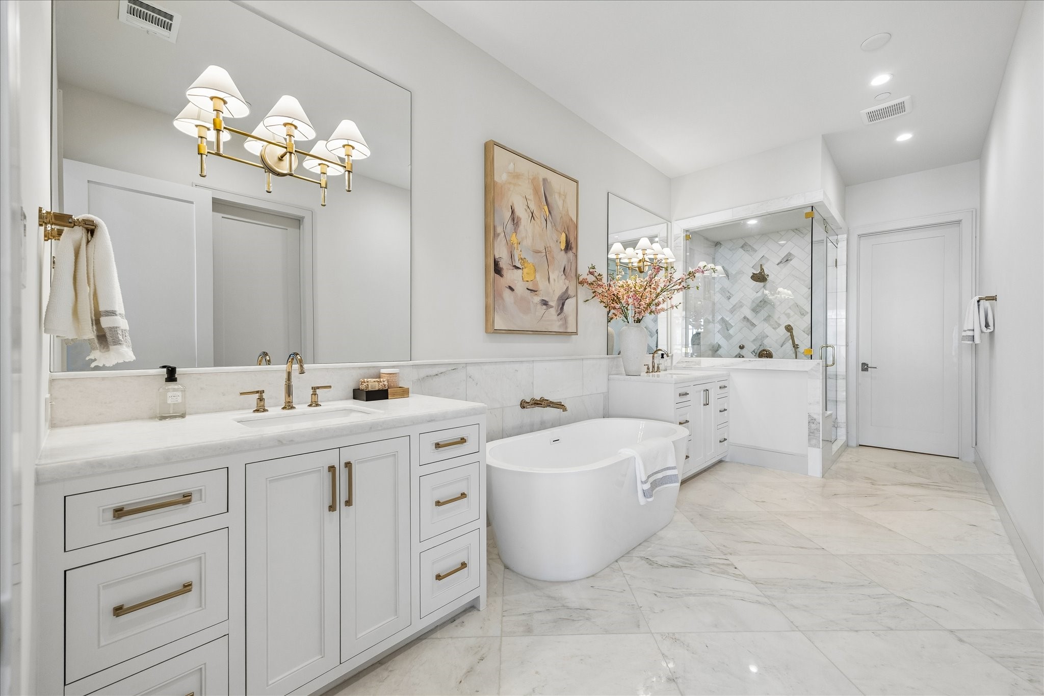 1215 West Pierce Street Houston, TX 77019 - Photo 22 of 37 Kalta Bianco polished marble makes the primary bathroom gleam. 24x24 tile flooring, large format brick design wainscoting, and herringbone shower accent wall keep the visual interest while tying together the look. The 67" Mermaid free-stading tub will be a joy to soak in. All the bathrooms feature the same on-site built, recessed panel cabinetry found in the kitchen.