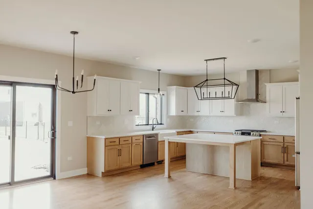 a kitchen with stainless steel appliances a stove a sink dishwasher a refrigerator and white cabinets with wooden floor