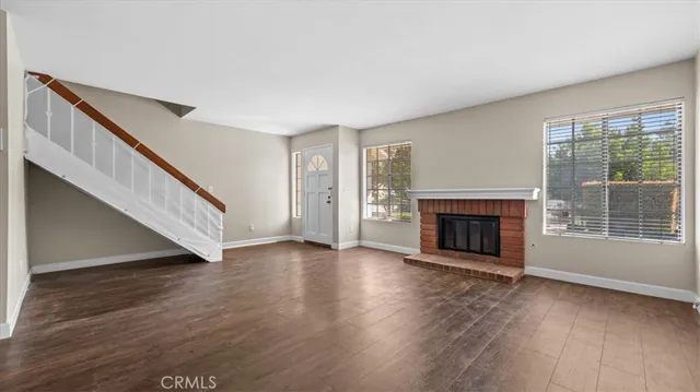 a view of an empty room with wooden floor fireplace and a window