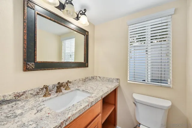 a bathroom with a granite countertop sink vanity mirror and toilet