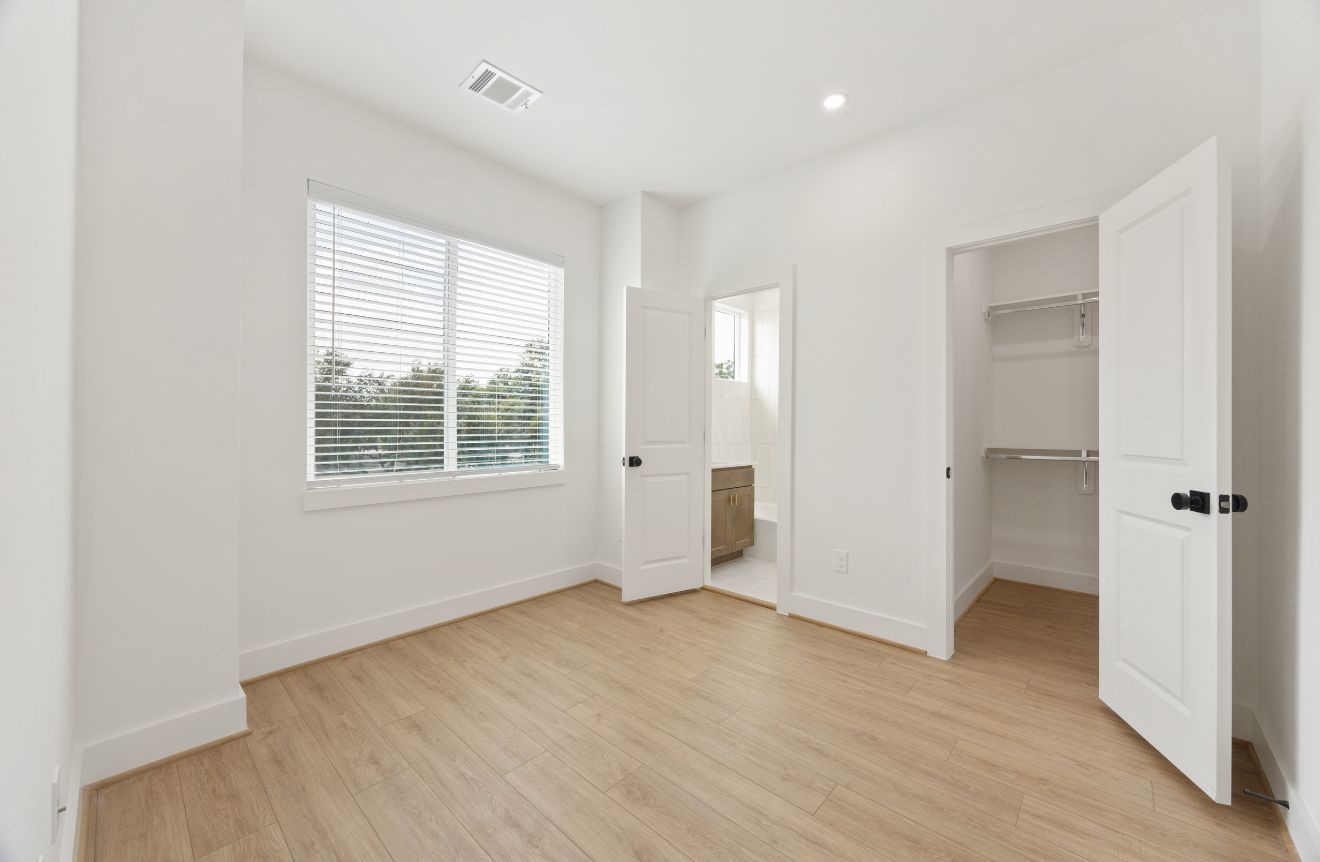 2121 Hoskins Drive, Unit C Houston, TX 77080 - Photo 30 of 34 Bright secondary bedroom with high ceilings, recessed lighting, large window, warm wood-look flooring, and direct access to a closet and nearby bath. The neutral finishes create a calm, versatile space that works beautifully as a bedroom, guest room, nursery, or private home office.