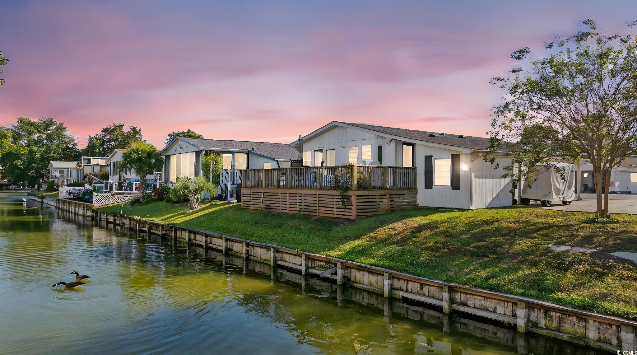 Back of house at dusk with a lawn and a deck with water view