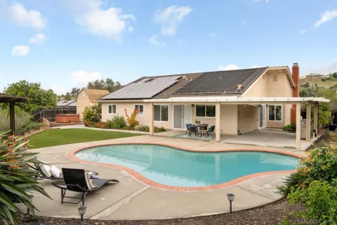 a white house with a large pool yard and dining table and chairs with wooden fence