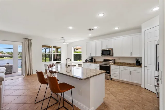 a kitchen with stainless steel appliances granite countertop a stove a sink a refrigerator white cabinets and chairs
