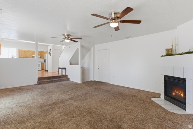 134 West 475 South Ogden, UT 84404 - Photo 9 of 27 Unfurnished living room featuring a tiled fireplace, light carpet, and a ceiling fan
