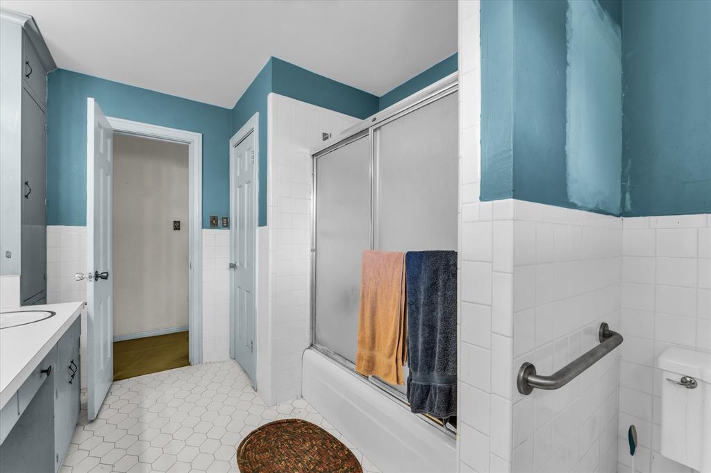 421 Rice Avenue Waco, TX 76708 - Photo 26 of 40 Upstairs; White hexagonal tile flooring, white tile wainscoting, built-in vanity with integrated sink, built-in storage cabinetry, and a bathtub with a sliding glass enclosure