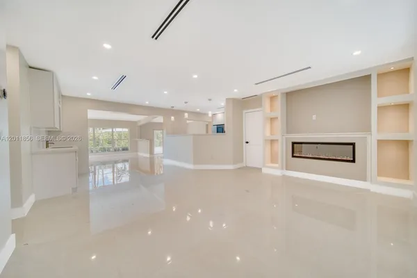 a view of an empty room with wooden floor and a kitchen