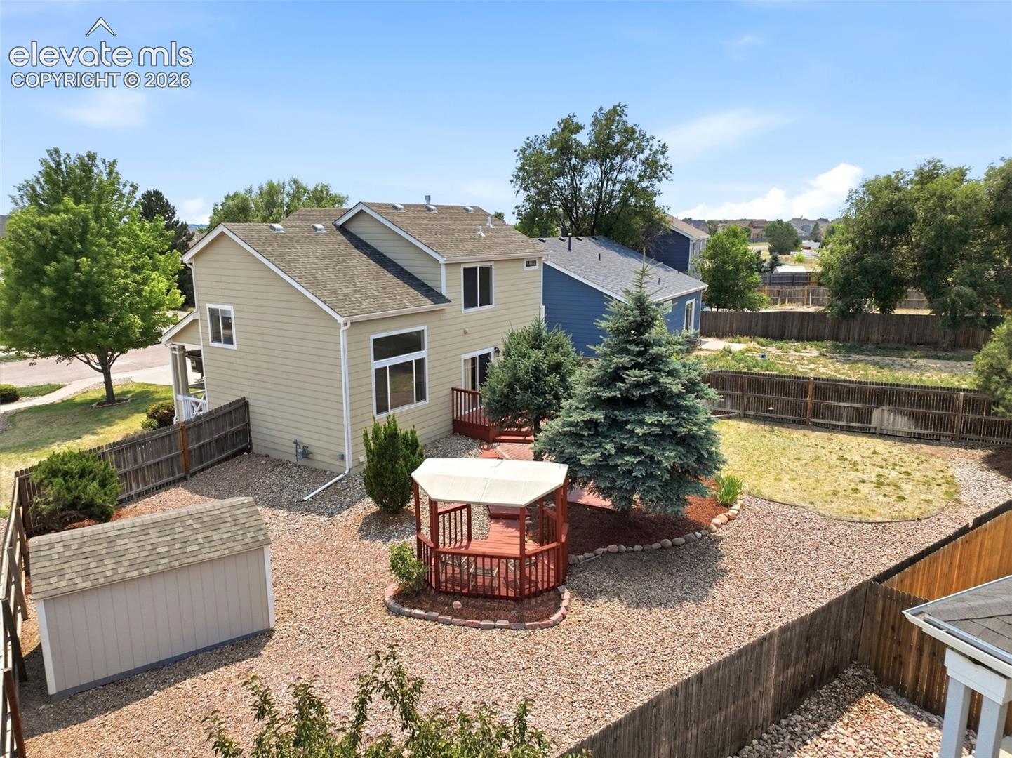 7904 Coffee Road Peyton, CO 80831 - Photo 40 of 48 Rear exterior featuring two-story construction, a spacious wooden deck, a gazebo with a white canopy, a storage shed, and mature landscaping