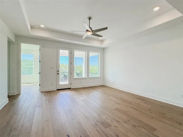 an empty room with wooden floor ceiling fan and windows