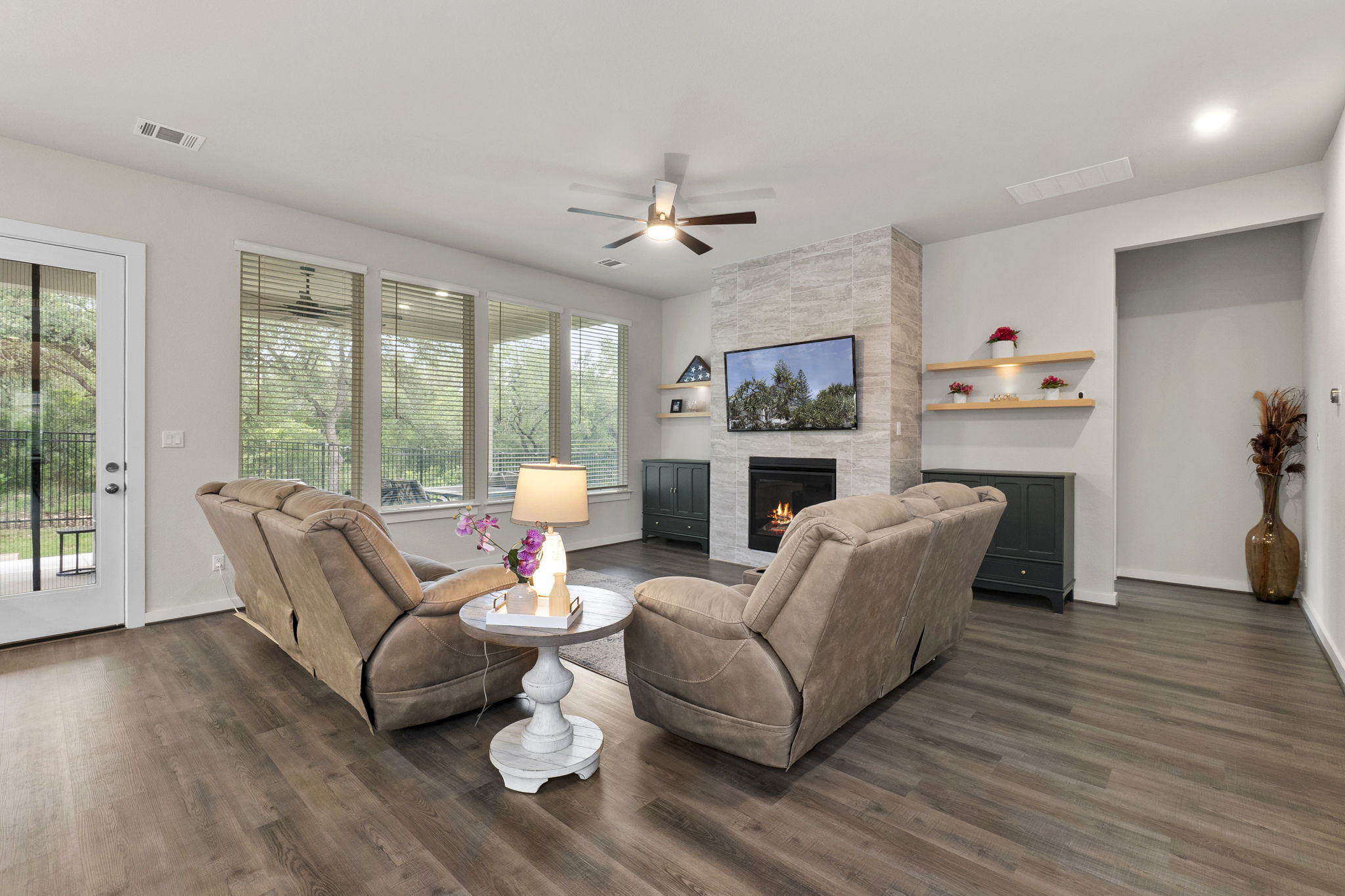 460 Constitution Way Kyle, TX 78640 - Photo 10 of 40 Living area featuring wood-finish flooring, a stone-accented fireplace, a ceiling fan, and multiple windows with blinds