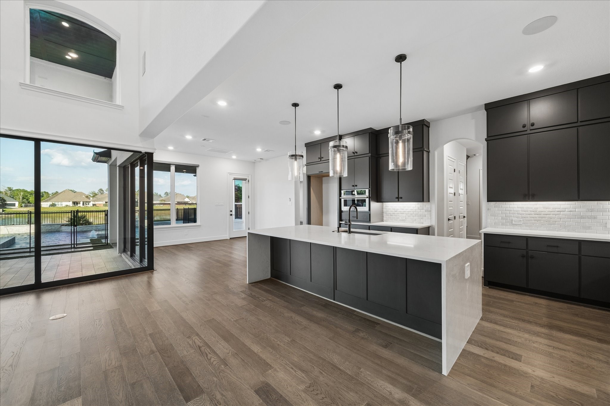 28015 Royal Swan Lane Spring, TX 77386 - Photo 11 of 25 Designer kitchen with a large island, sleek cabinetry, stainless steel appliances, and pendant lighting, flowing into a bright breakfast area with corner sliding doors that open to the covered patio and pool for seamless indoor–outdoor living.