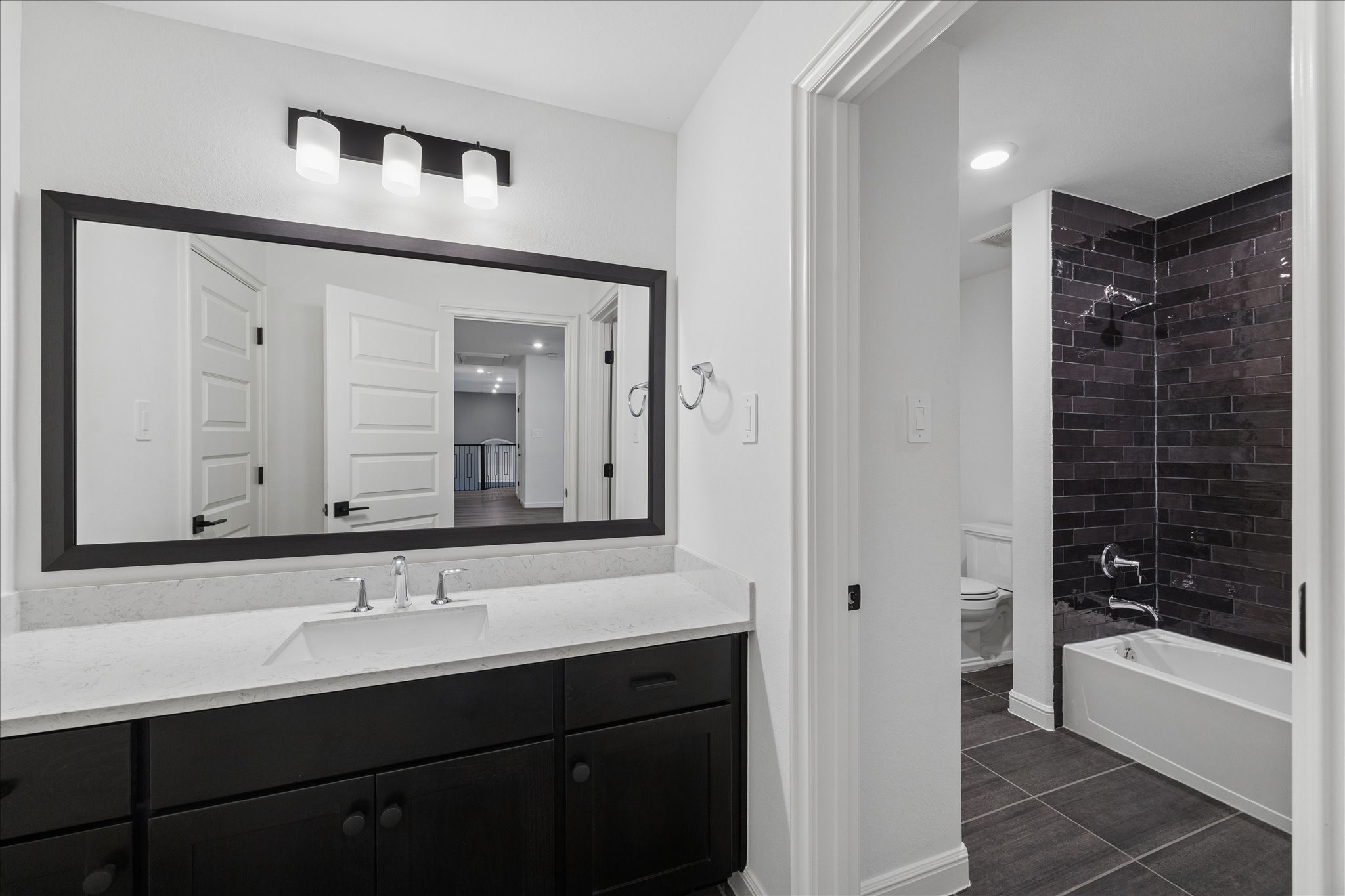 28015 Royal Swan Lane Spring, TX 77386 - Photo 18 of 25 Jack & Jill bathroom featuring a spacious vanity with quartz countertops, sleek black cabinetry, and a striking tiled tub/shower surround. Functional layout offers convenient access from adjoining bedrooms.