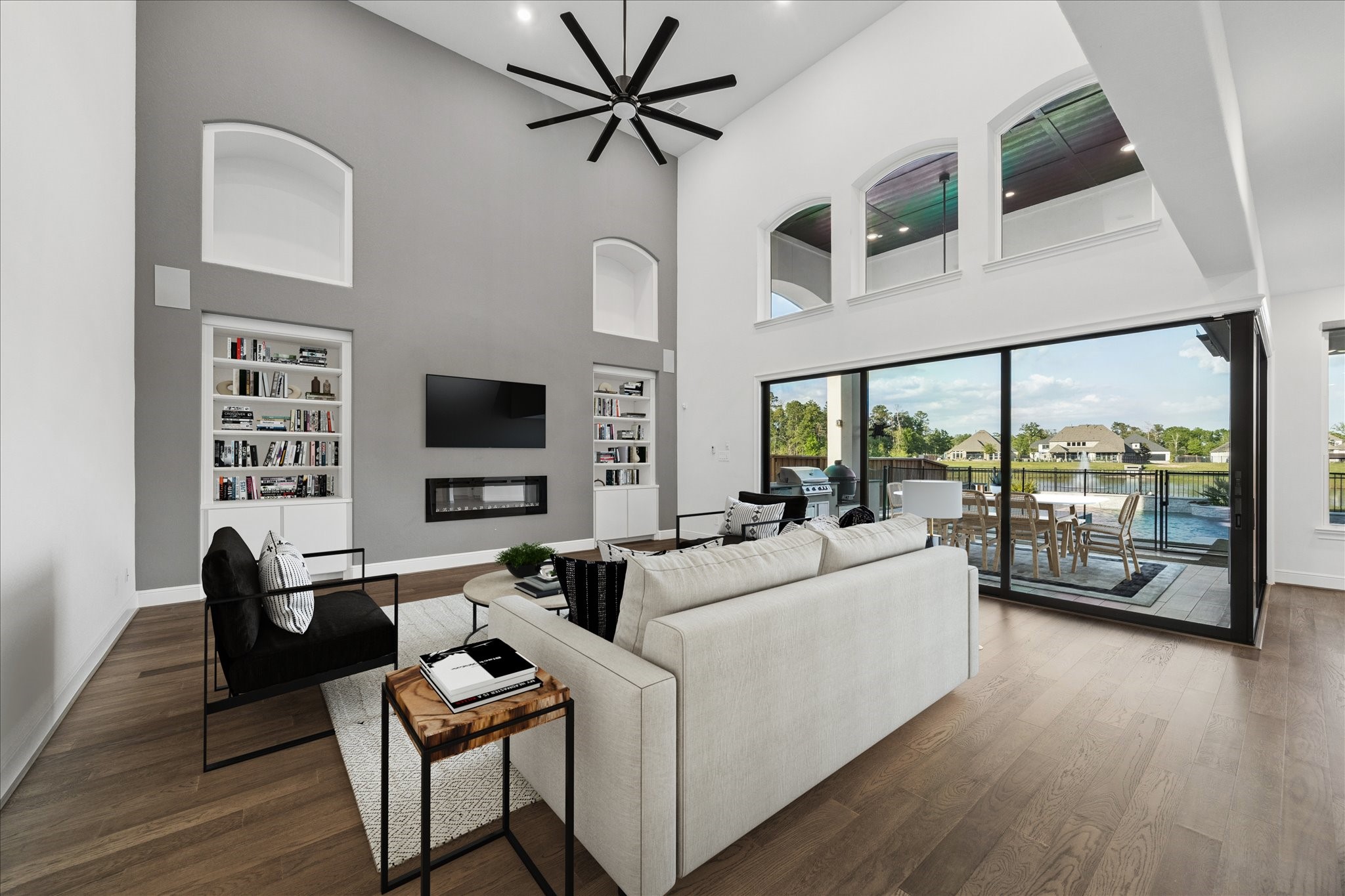 28015 Royal Swan Lane Spring, TX 77386 - Photo 8 of 25 Light-filled living room with soaring ceilings, built-in shelving, and expansive 90-degree sliding glass doors creating seamless indoor-outdoor living. Stunning views of the pool and water beyond enhance the bright, open atmosphere. *Virtually Staged