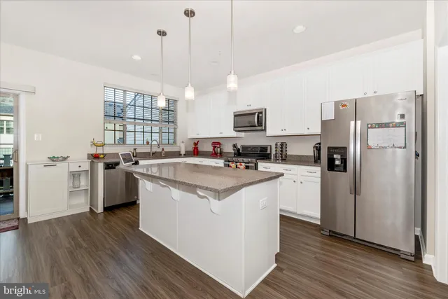 a kitchen with stainless steel appliances a stove a refrigerator a sink a oven and white cabinets with wooden floor