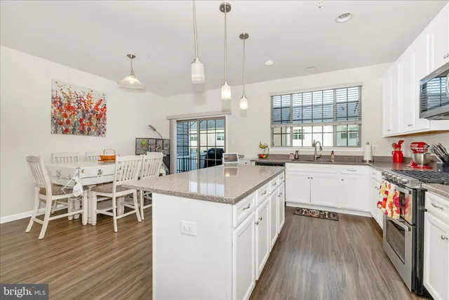 a open kitchen with stainless steel appliances granite countertop a stove oven a dining table and chairs with wooden floor