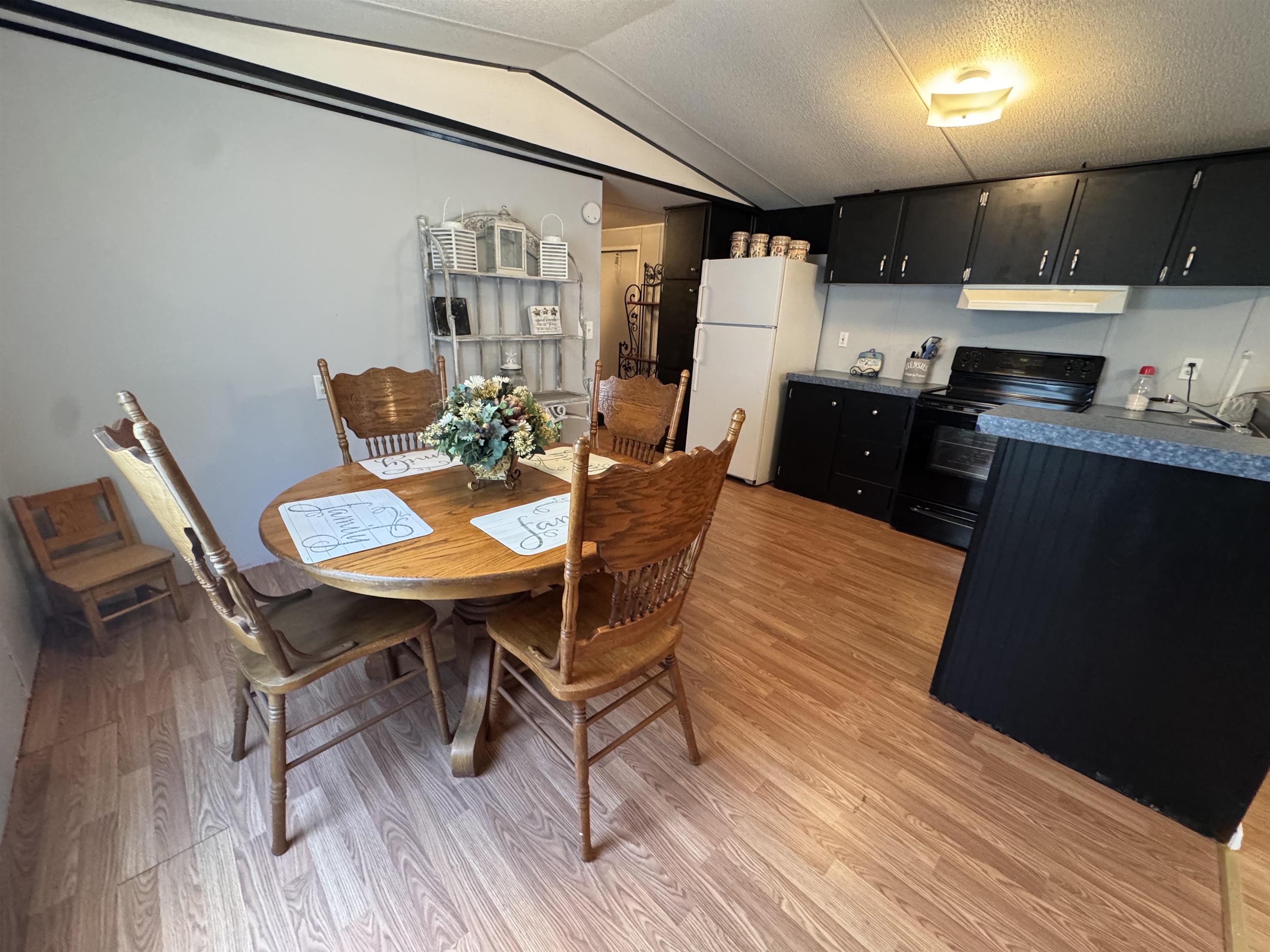 2511 Watkins Road Michie, TN 38357 - Photo 13 of 40 Open-concept kitchen and dining area featuring wood-finish flooring, black cabinetry, white refrigerator, and a black range