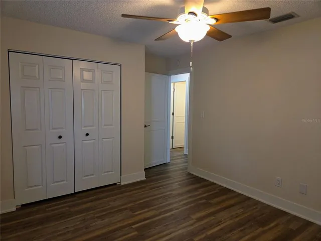 a view of an empty room with wooden floor and a chandelier fan