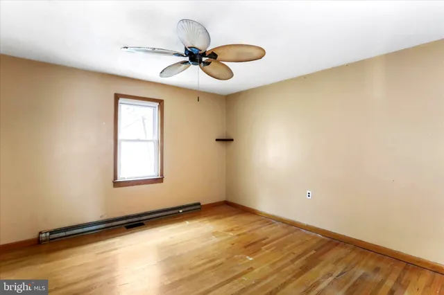 a view of an empty room with wooden floor and a ceiling fan