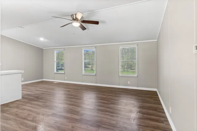 an empty room with wooden floor fan and windows