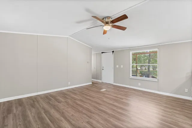 an empty room with wooden floor fan and windows