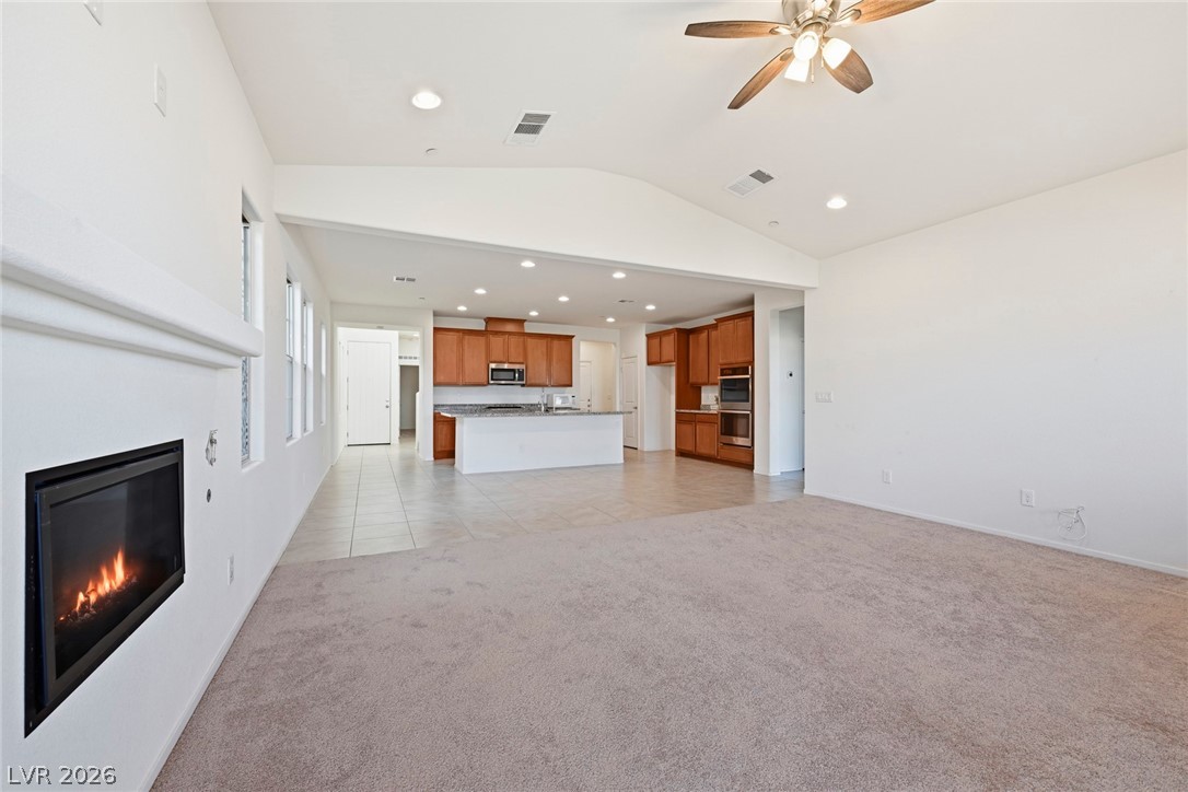 250 Dedication Avenue Henderson, NV 89011 - Photo 8 of 67 Unfurnished living room with recessed lighting, a glass covered fireplace, a ceiling fan, light colored carpet, and lofted ceiling