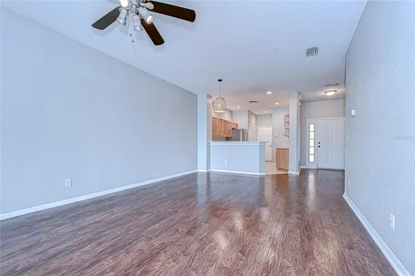 an empty room with wooden floor chandelier fan and windows