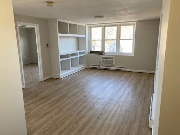 an empty room with wooden floor closet and windows