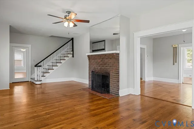 an empty room with wooden floor a fireplace a ceiling fan and windows