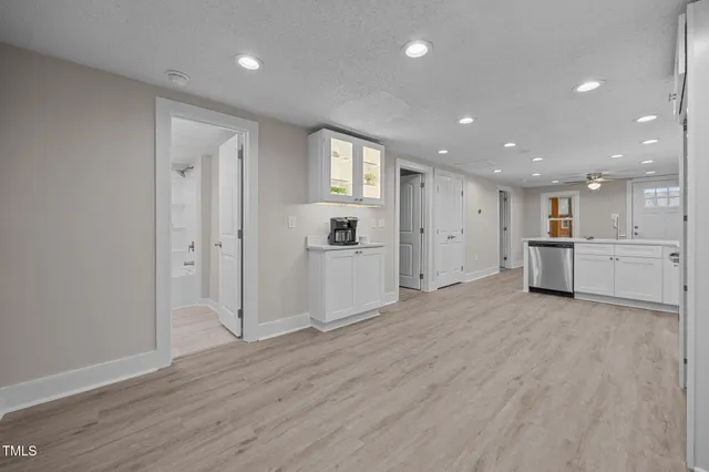 a view of an empty room with wooden floor kitchen view and a window