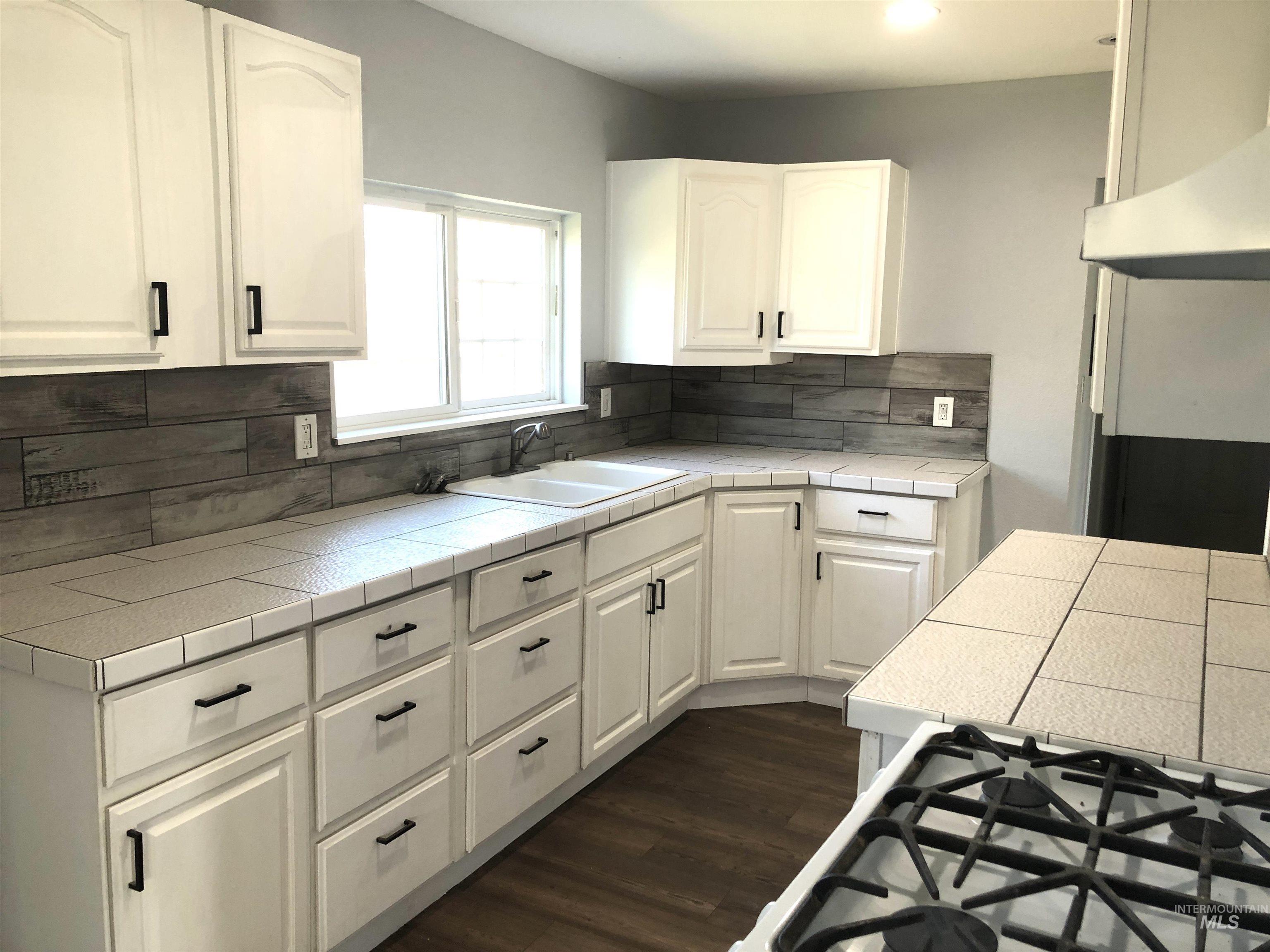 717 10th Street Clarkston, WA 99403 - Photo 6 of 23 Kitchen featuring dark wood-style floors, exhaust hood, white cabinetry, and tile counters