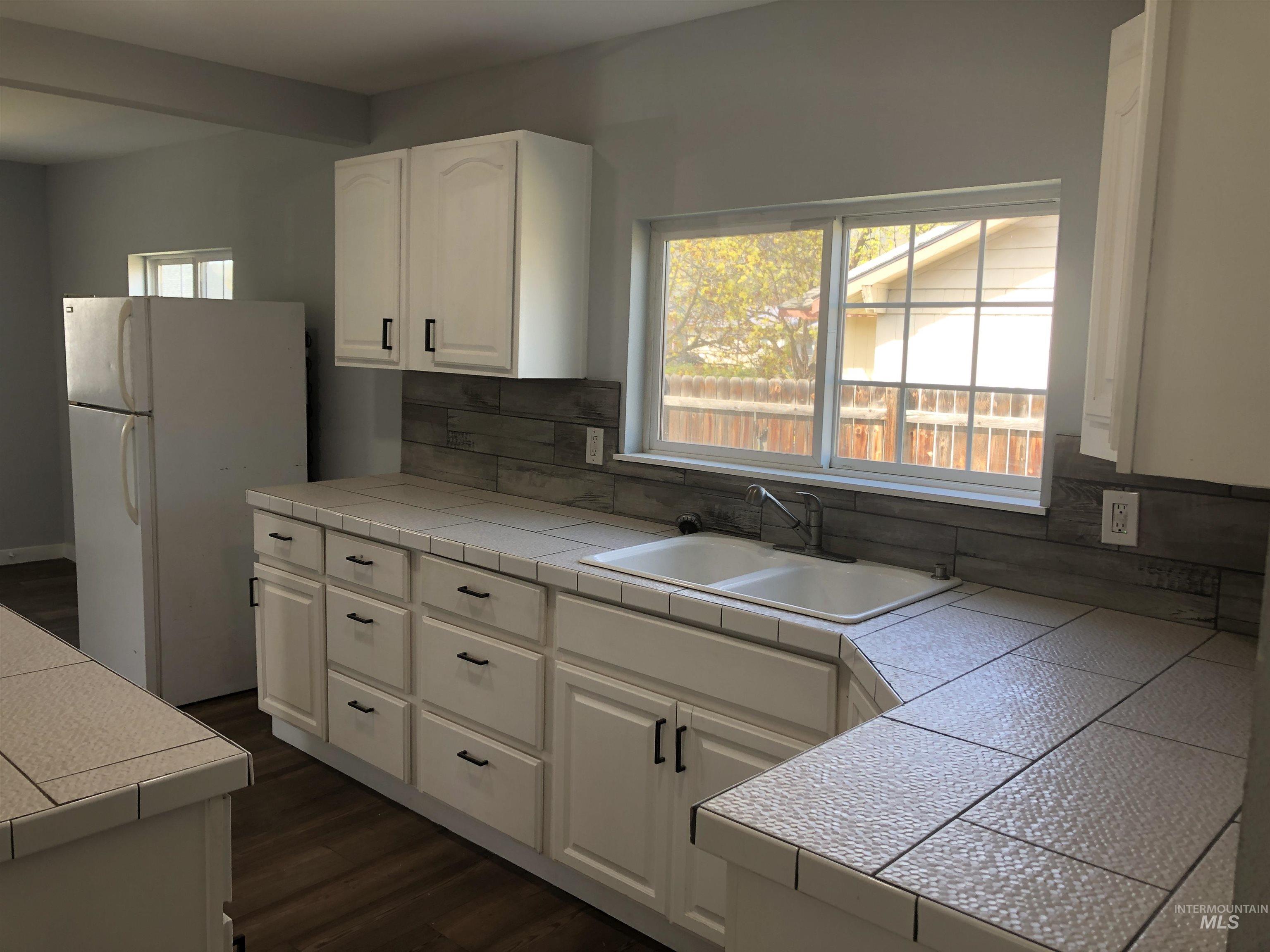 717 10th Street Clarkston, WA 99403 - Photo 8 of 23 Kitchen with tile counters, backsplash, freestanding refrigerator, white cabinetry, and dark wood-type flooring