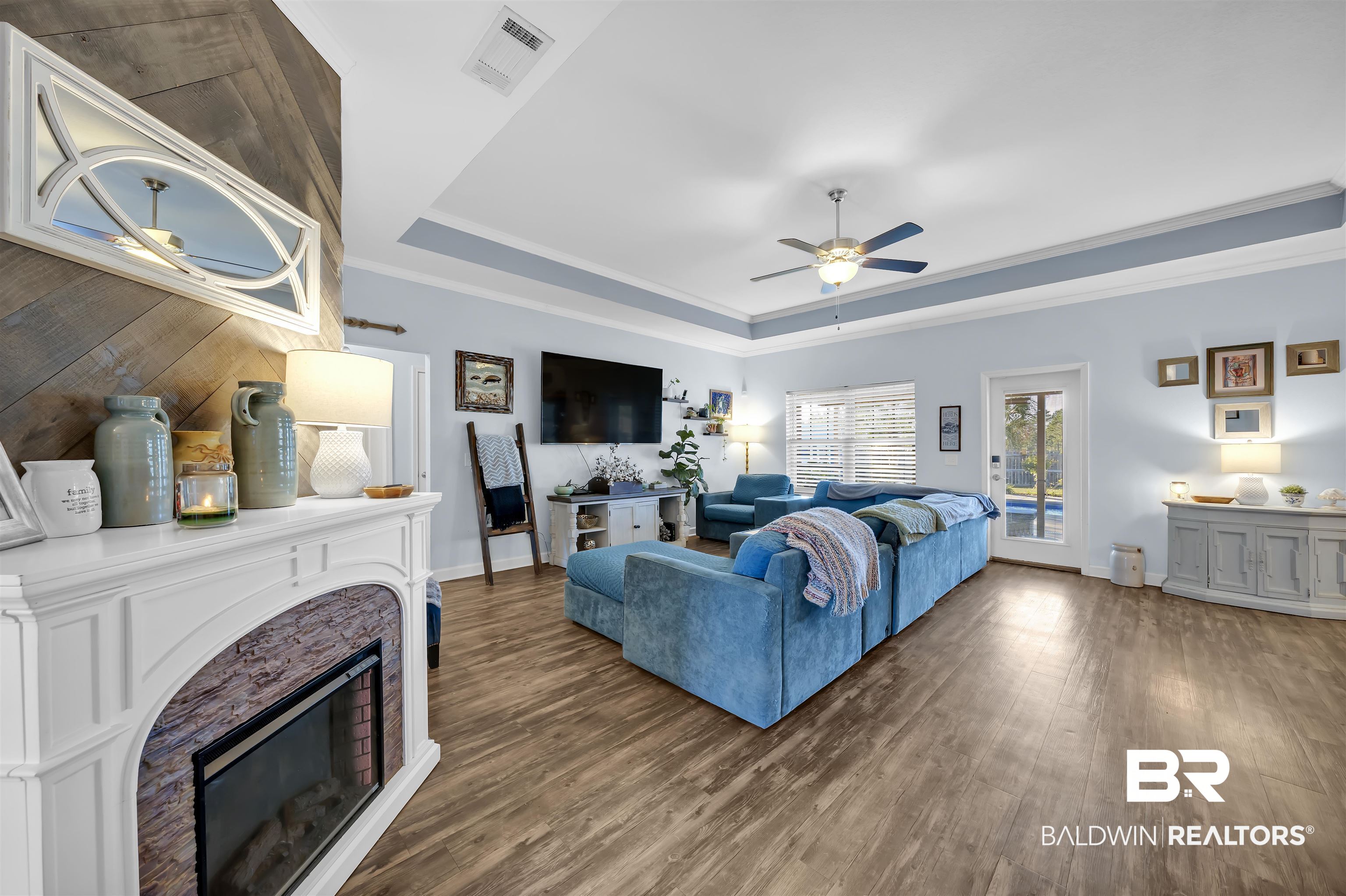 10180 Lyttleton Loop Lillian, AL 36549 - Photo 10 of 37 Living area featuring a stone fireplace, a tray ceiling, dark wood-type flooring, crown molding, and ceiling fan