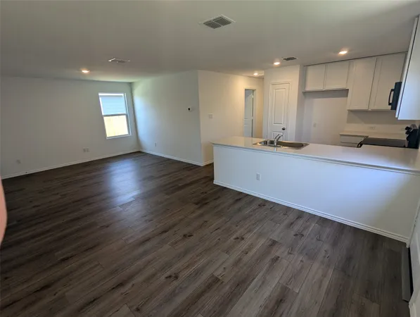 a kitchen with white cabinets a sink a stove a wooden floor and entryway