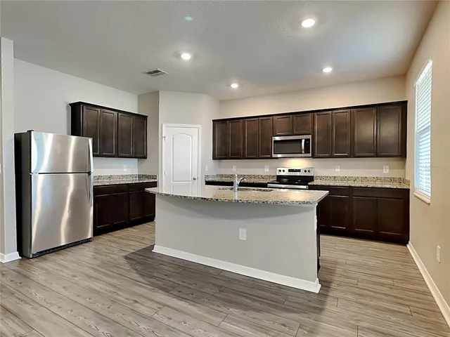 a kitchen with stainless steel appliances granite countertop a refrigerator a stove top oven a sink and dishwasher with wooden floor