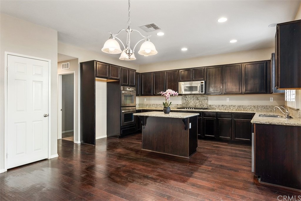 46945 Peach Tree Street Temecula, CA 92592 - Photo 7 of 32 a kitchen with stainless steel appliances granite countertop a refrigerator a sink dishwasher a stove top oven a kitchen island with wooden floor and cabinets