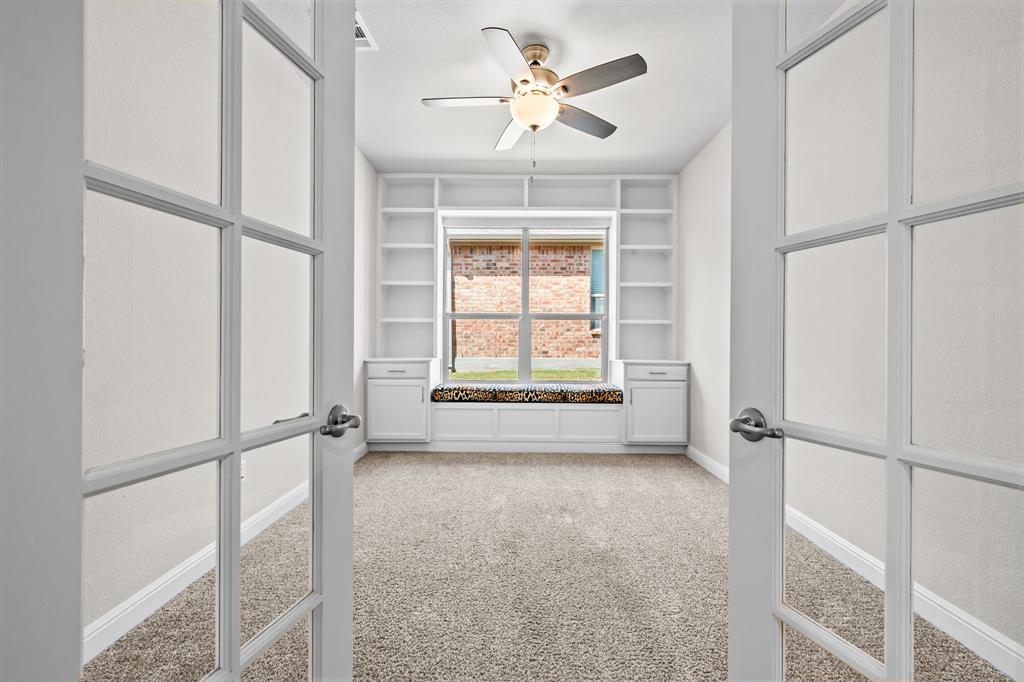 1840 Ruffian Road Granbury, TX 76049 - Photo 16 of 33 French doors opening to a versatile room with carpet flooring, built-in shelving, a window seat with storage, and a ceiling fan with integrated lighting