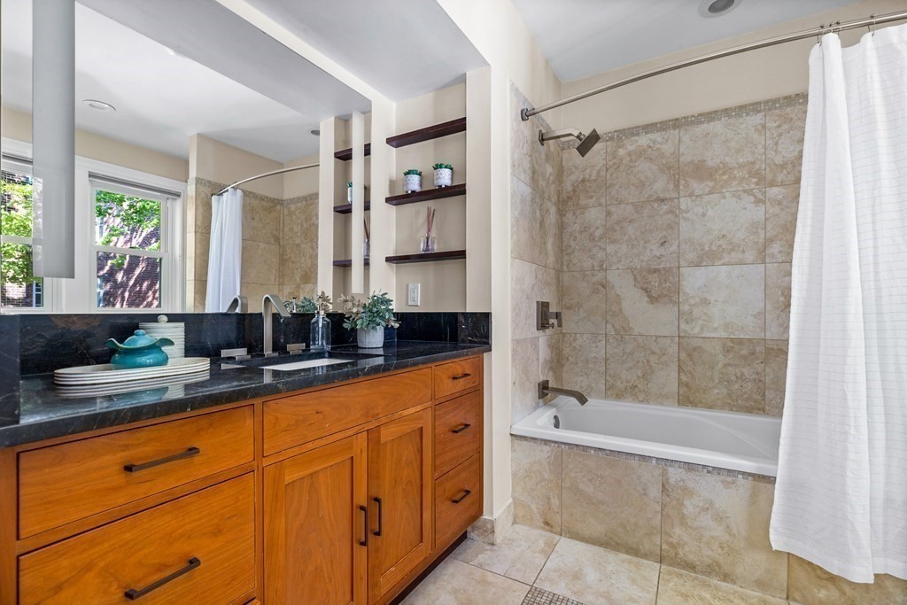 87 Coolidge Street, Unit 2 Brookline, MA 02446 - Photo 13 of 34 a bathroom with a granite countertop sink a mirror a bathtub and shower