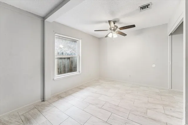 an empty room with chandelier fan and windows