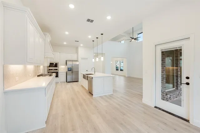 a large white kitchen with kitchen island a stove a sink a refrigerator and cabinets