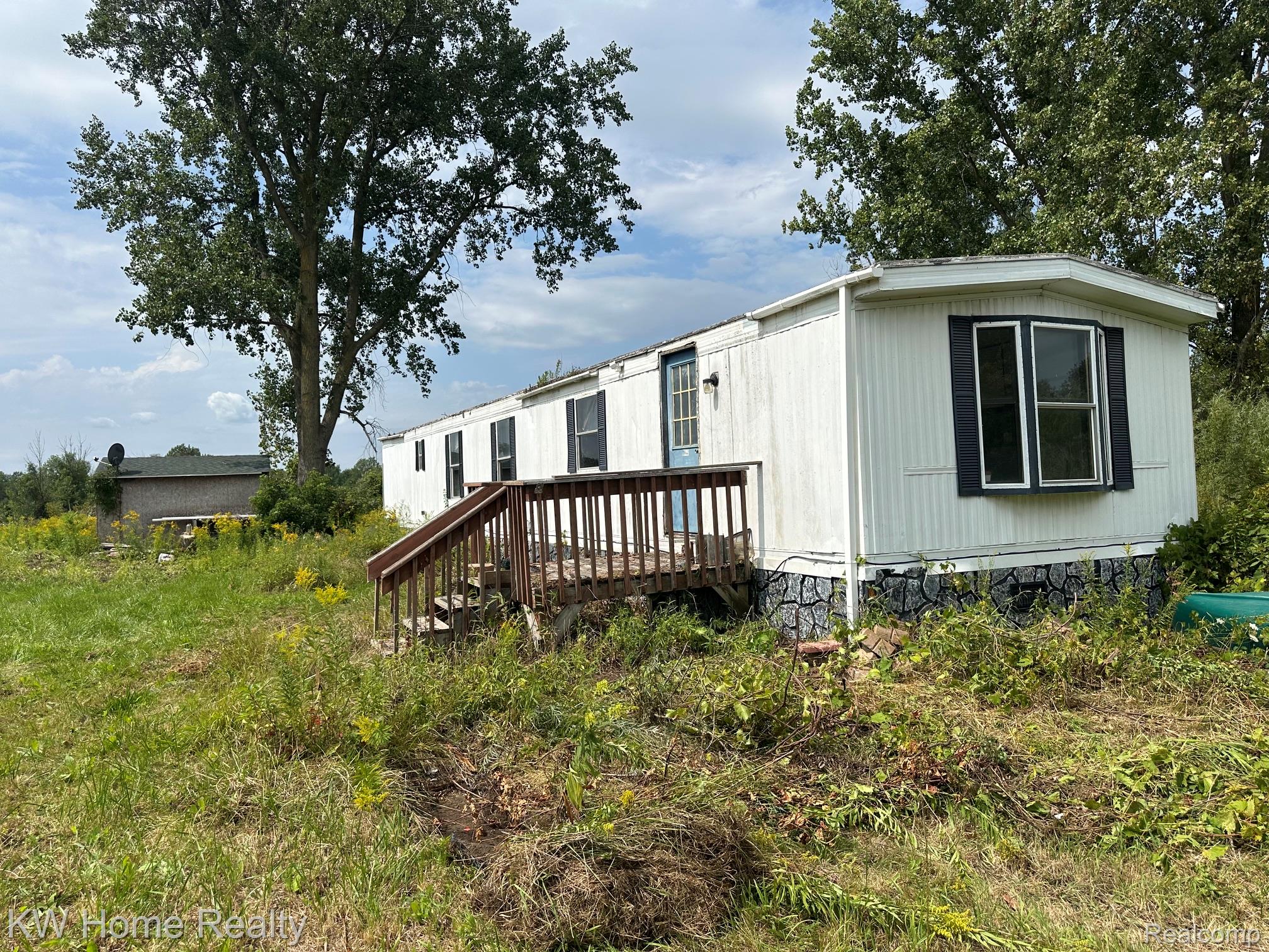 2911 Sanilac Road Caro, MI 48723 - Photo 2 of 8 White siding exterior with a dark-trimmed bay window, wood deck, and a secondary structure