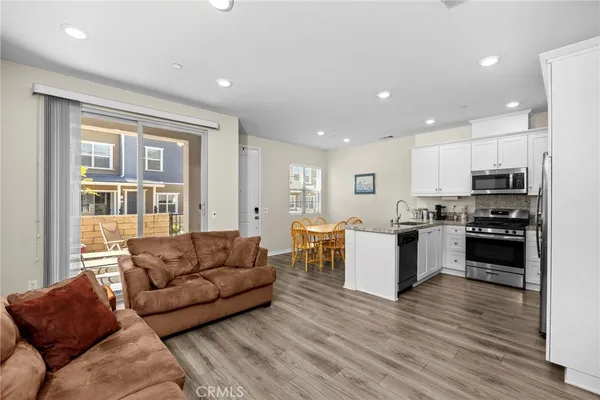 a kitchen with stainless steel appliances granite countertop a refrigerator a stove top oven a sink dishwasher a dining table and chairs with wooden floor