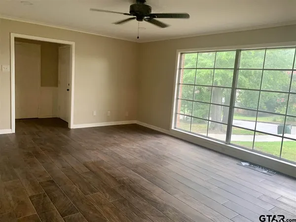 an empty room with wooden floor fan and windows