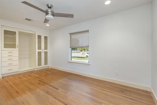 an empty room with wooden floor fan and windows