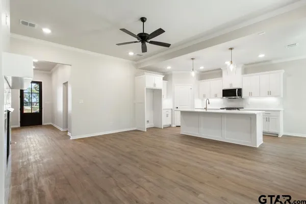 a view of an empty room with wooden floor and a ceiling fan