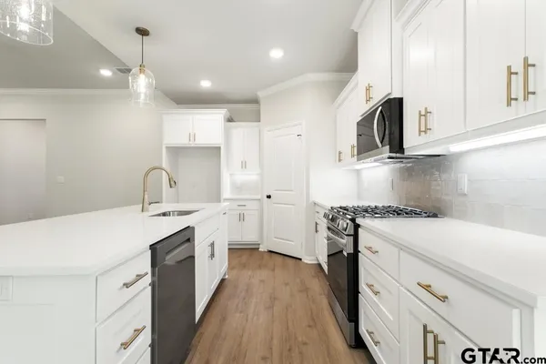 a kitchen with stainless steel appliances granite countertop a sink a microwave oven a refrigerator and white cabinets with wooden floor