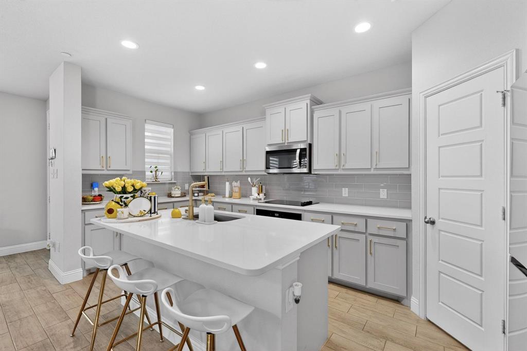 The property features a kitchen with light-colored cabinetry, a large central island with seating, stainless steel appliances, and wood-look tile flooring