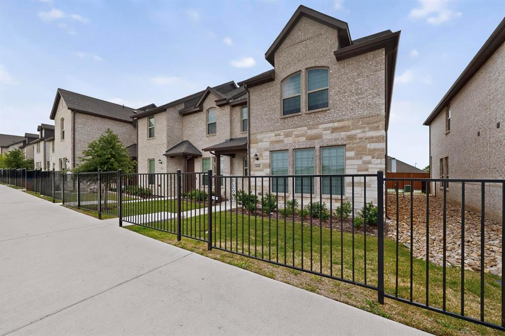 6040 Bursey Road Watauga, TX 76148 - Photo 6 of 39 This property features a brick and stone exterior, visible windows, and a well-maintained lawn area behind a black metal fence
