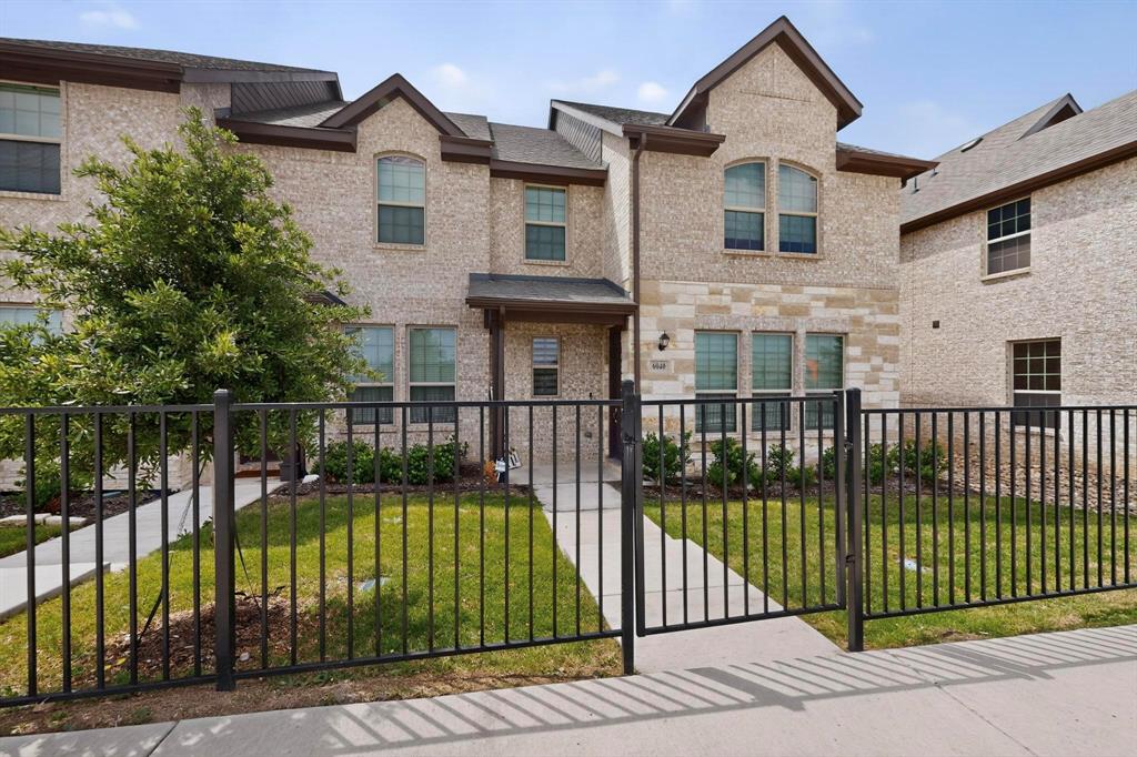 6040 Bursey Road Watauga, TX 76148 - Photo 7 of 39 This property features a brick and stone facade, a well-maintained lawn, and a black metal fence with a gate