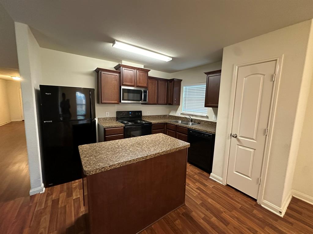 1818 Clegg Street Howe, TX 75459 - Photo 21 of 34 Kitchen featuring wood-finish flooring, dark wood cabinetry, granite-style countertops, stainless steel microwave, and a central island